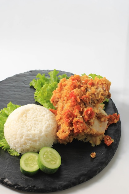 Ayam Geprek è il cibo di strada popolare in Indonesia. Fatto da pollo croccante schiacciato in Sambal Bawang (salsa di peperoncino e aglio). Servito con Riso e Verdure