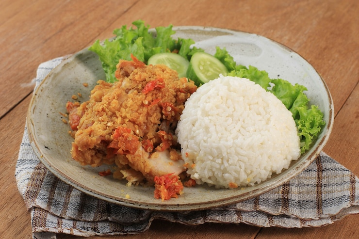 Ayam Geprek è il cibo di strada popolare in Indonesia. Fatto da pollo croccante schiacciato in Sambal Bawang (salsa di peperoncino e aglio). Servito con Riso e Verdure