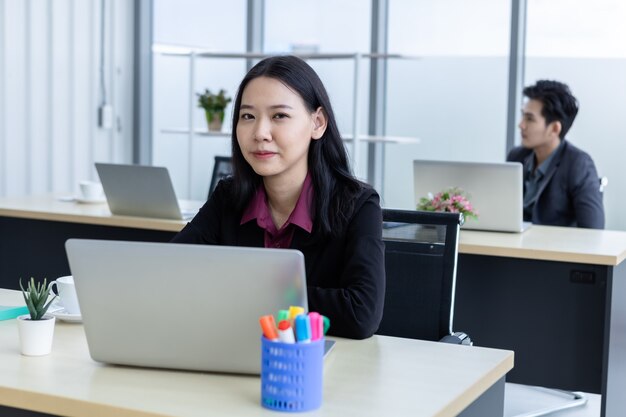 Azienda di successo, dirigente Felice di sorridere Giovane donna d'affari asiatica sul posto di lavoro che lavora con il computer portatile del personale dell'ufficio non è felice con i colleghi di lavoro dietro in ufficio