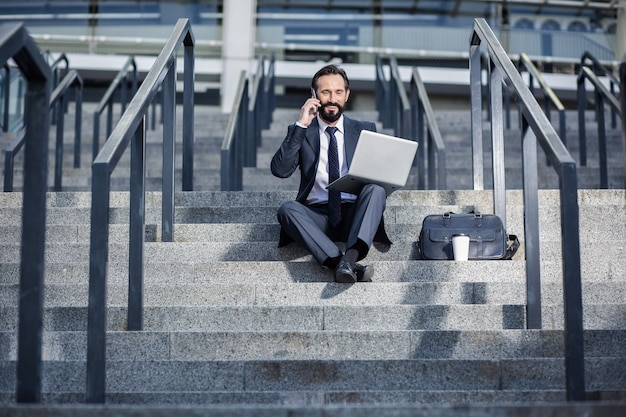 Azione supplementare. Uomo d'affari professionista ottimista che ha una conversazione sul telefono mentre era seduto sulle scale