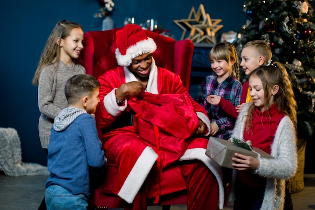 Babbo Natale africano seduto in poltrona e dando i regali ai bambini piccoli