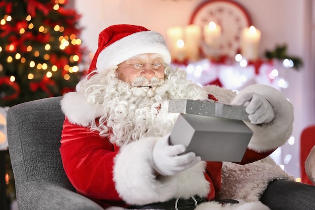 Babbo Natale autentico con scatola regalo seduto in poltrona nella stanza decorata per Natale