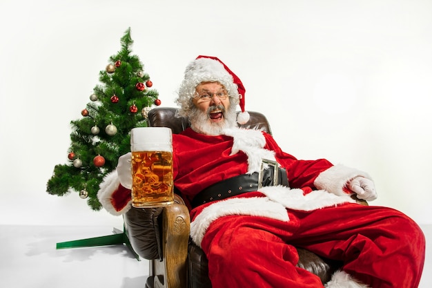 Babbo Natale che beve birra vicino all'albero di Natale congratulandosi sembra ubriaco e felice