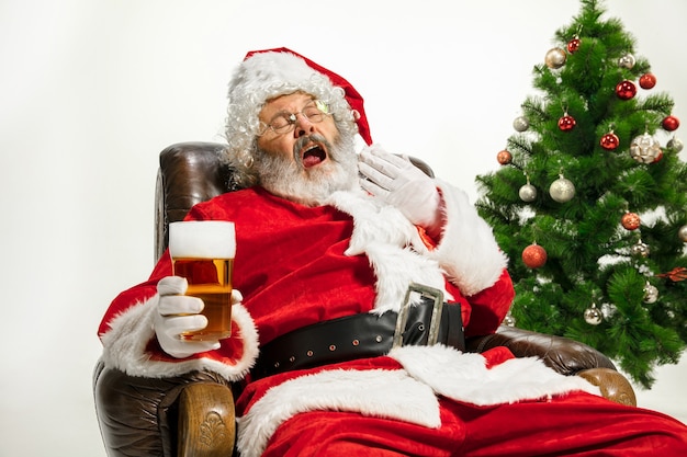 Babbo Natale che beve birra vicino all'albero di Natale congratulandosi sembra ubriaco e felice
