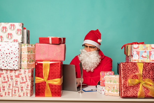 Babbo Natale che indossa il cappello lavora nel suo ufficio con i regali, preparandosi per le vacanze.