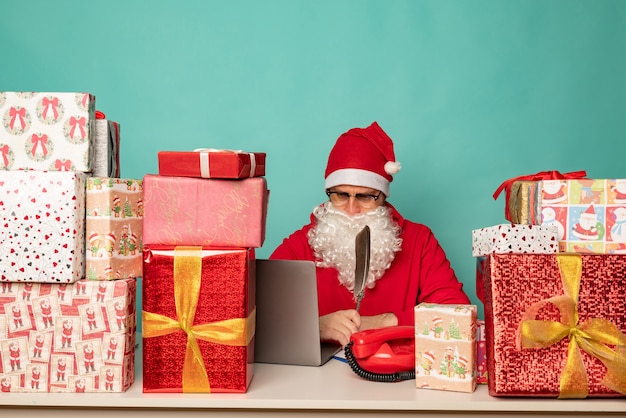 Babbo Natale che indossa un cappello lavora nel suo ufficio con i regali, preparandosi per le vacanze.