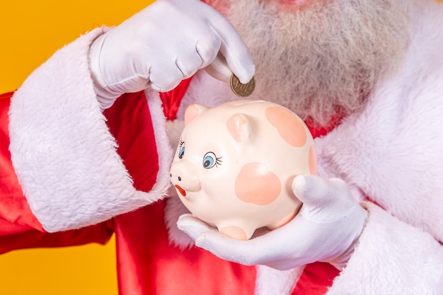 Babbo Natale che mette una moneta in un salvadanaio in ceramica. Concetto di risparmio per la fine dell'anno. Spesa nel periodo natalizio. Speso per i regali di Natale.