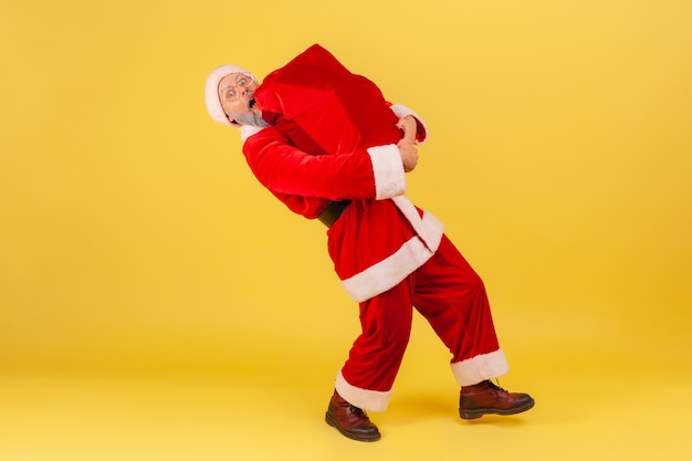 Babbo natale che porta una grande borsa pesante con regali di Natale, congratulandosi con il nuovo anno.