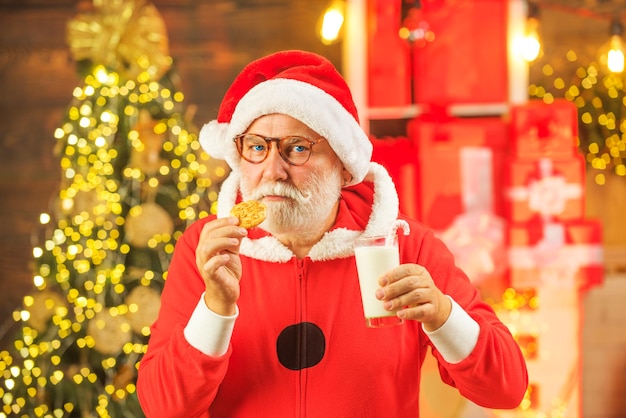 Babbo Natale che tiene biscotto e bicchiere di latte su sfondo albero di natale babbo natale godendo in servito g...