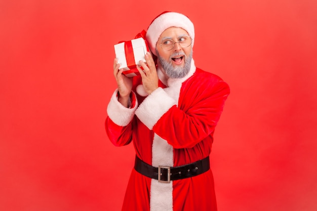 Babbo Natale che tiene e scuote una scatola avvolta con un regalo di Natale, pensa a cosa c'è dentro.