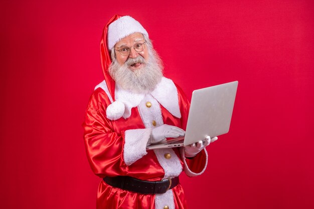 Babbo Natale che utilizza un computer portatile su sfondo rosso.