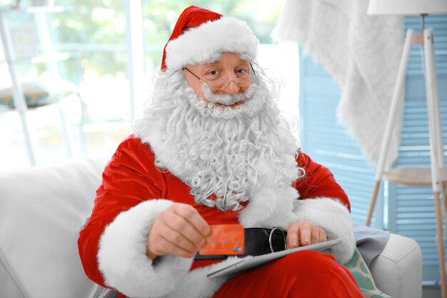 Babbo Natale con carta di credito e tablet sul divano di casa