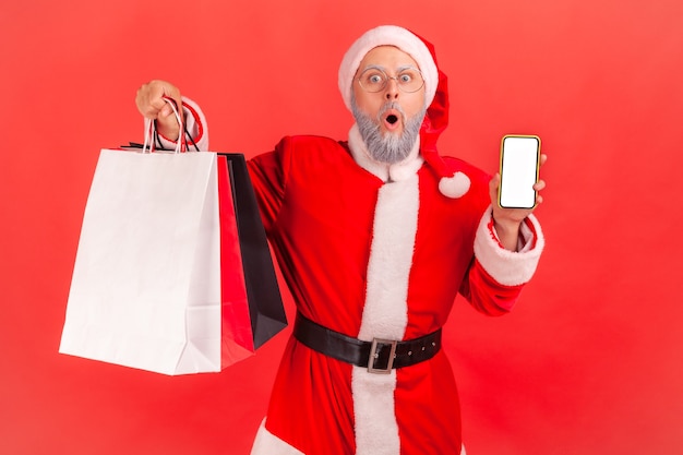 Babbo natale con in mano borse della spesa e telefono con display vuoto, scioccato dagli sconti natalizi