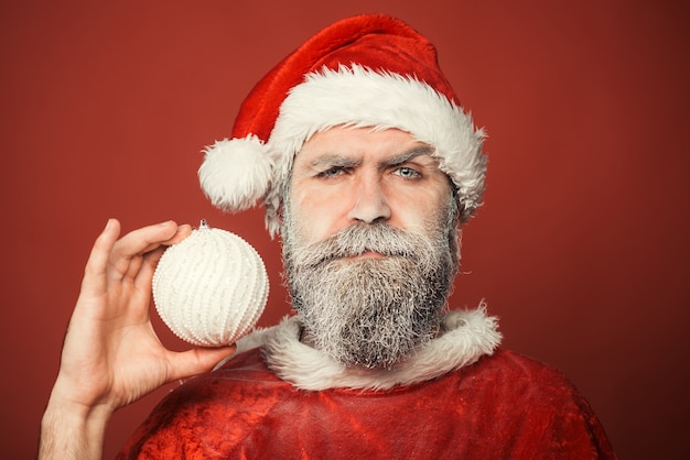 Babbo natale con la barba lunga in abiti rossi e cappello di capodanno tiene la palla di natale decorativa capodanno