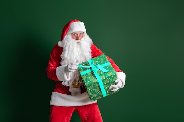 Babbo Natale con la barba lunga tiene un'enorme confezione regalo verde su sfondo verde mentre guarda la fotocamera