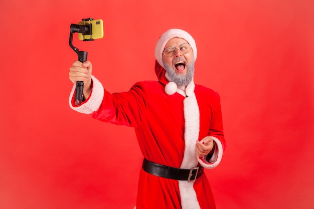 Babbo natale con steadicam in mano, livestream, guardando lo schermo del telefono e urlando.