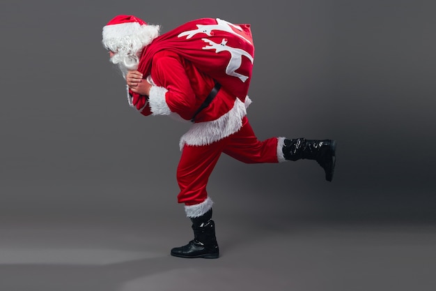 Babbo Natale corre con la borsa con i regali di Natale sulla schiena su fondo bianco. .