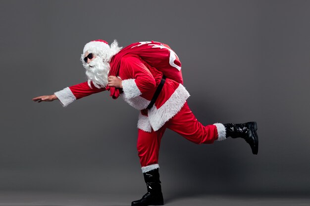 Babbo Natale corre con la borsa con i regali di Natale sulla schiena su fondo bianco. .