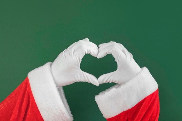 Babbo Natale due mani che fanno a forma di cuore gesto isolato su sfondo verde primo piano segno di amore approvazione congratulazioni natalizie come schermo chiave Chroma mani guantate bianche forma un cuore