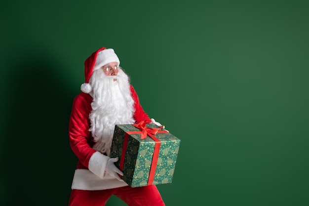 Babbo Natale emotivo che si intrufola mentre tiene in mano una grande scatola regalo verde su sfondo verde dello studio