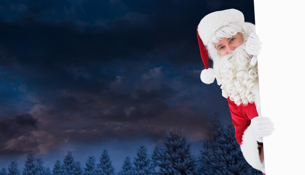 Babbo Natale felice che tiene poster contro il cielo notturno sopra la foresta