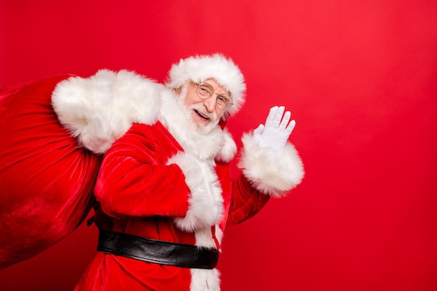 Babbo Natale in bretelle e cappello in posa sulla parete rossa