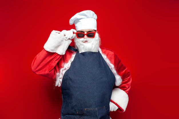 Babbo Natale in cappello da chef e grembiule su sfondo rosso cuoco maschio in costume da Babbo Natale
