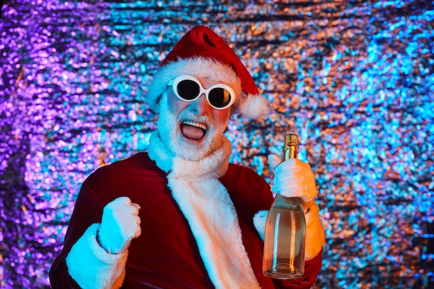 Babbo Natale in costume rosso e occhiali da sole che tiene una bottiglia di champagne e celebra il nuovo anno