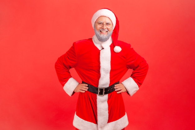 Babbo natale in piedi con le mani sui fianchi che guarda l'obbiettivo con felice espressione.