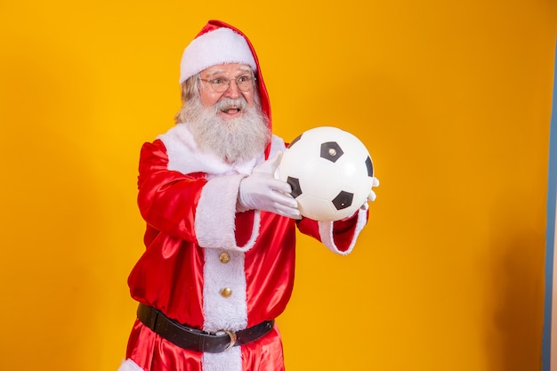 Babbo Natale in possesso di un pallone da calcio su sfondo giallo.