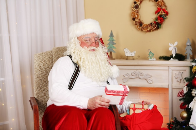 Babbo Natale seduto con i regali dei bambini su una sedia comoda vicino al caminetto a casa