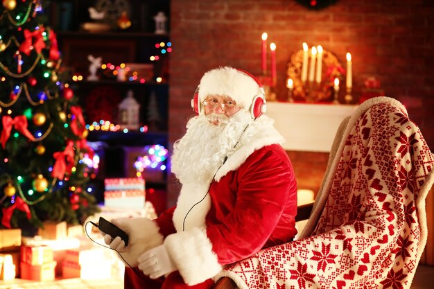 Babbo Natale seduto con le cuffie seduto su una comoda sedia a dondolo a casa