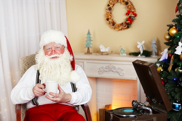 Babbo Natale seduto con una tazza di bevanda calda su una sedia comoda vicino al caminetto a casa