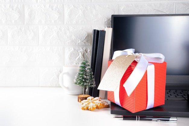 Babbo Natale segreto. Celebrazione di Natale in ufficio. Scrivania da ufficio con laptop, taccuini, forniture per ufficio, smartphone e grande confezione regalo di Natale con fiocco festivo. flatlay