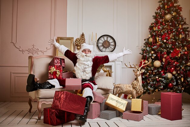 Babbo Natale si è sdraiato sul divano con un mucchio di regali vicino al camino e all'albero di Natale. Anno nuovo e buon Natale, concetto di buone feste