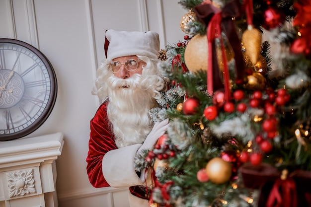 Babbo Natale si nasconde dietro l'albero di Natale per nascondere i regali. Concetto di vacanze di Capodanno e Buon Natale