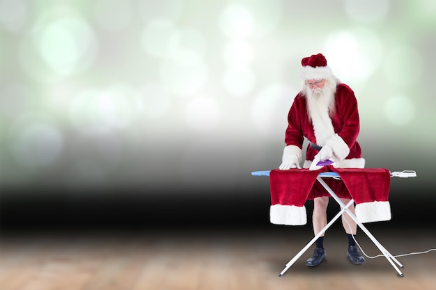 Babbo Natale si sta stirando i pantaloni contro un disegno luminoso scintillante sopra le assi