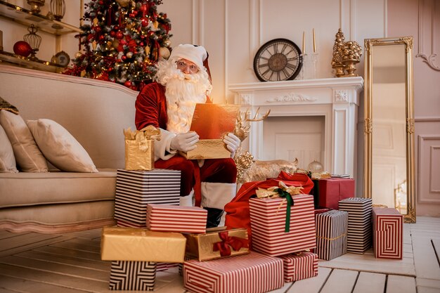 Babbo Natale sorpreso con un regalo magico incandescente vicino al bellissimo albero di Natale. Anno nuovo e buon Natale, concetto di buone feste