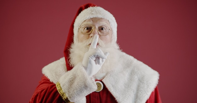 Babbo Natale tiene l'indice vicino alla bocca e guarda la telecamera Shh