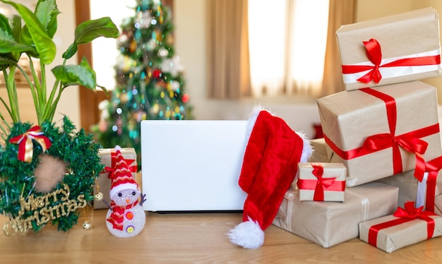 Babbo Natale ufficio in casa che si prepara per il Natale, molti regali e albero di Natale sullo sfondo, laptop sul tavolo, scrivania di Capodanno a casa, mock up