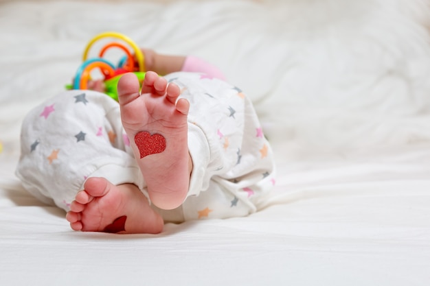 Baby foots con cuori in piedi Un neonato è sdraiato sul letto e gioca con i giocattoli