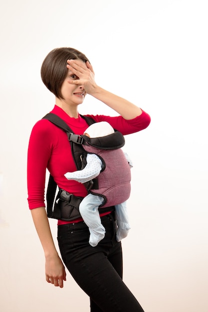 Babywearing confusa giovane madre con bambino in un marsupio scadente. Isolato su bianco.