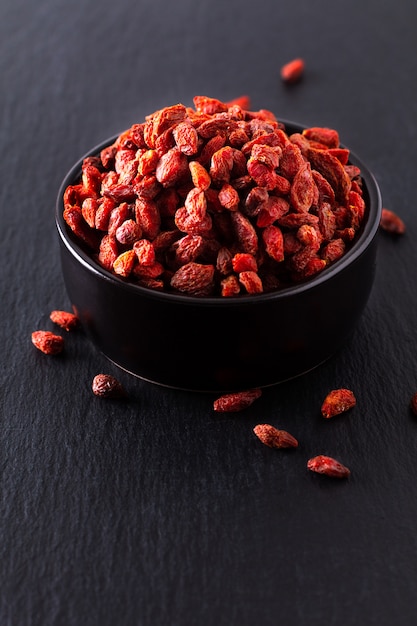 Bacca di Goji secca super cibo per il cervello in tazza di ceramica nera su lastra di pietra ardesia