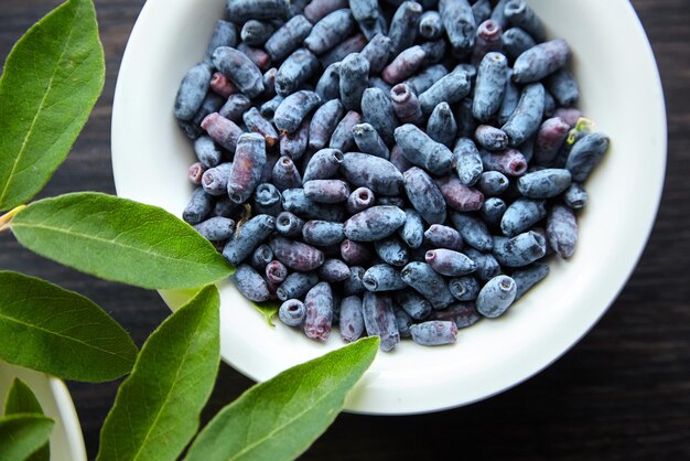 Bacca di Haskap con foglie verdi fresche in una ciotola bianca sulla vista del piano del tavolo Honeyberry Lonicera caerulea