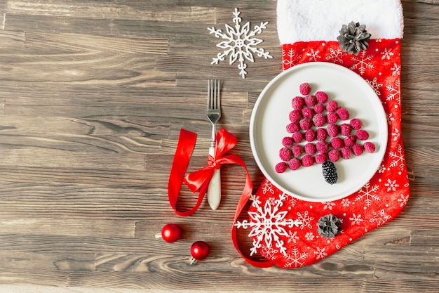 Bacca di lampone fresca dolce a forma di albero di Natale divertente sul piatto, calzino rosso su fondo di legno per la prima colazione dei bambini dei bambini. cibo di natale con decorazioni di capodanno, copia spazio