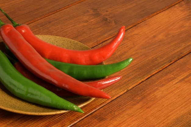 Baccelli di peperoncino rosso e verde giacciono a sinistra sparsi su un piatto di ceramica marrone su un tavolo di legno marrone wooden