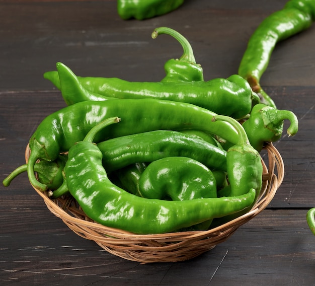 Baccelli di peperoncino verde in un cesto di vimini rotondo su un tavolo in legno marrone, vista dall'alto