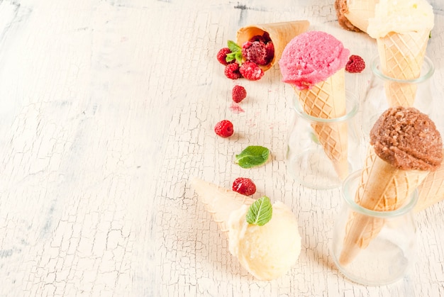 Bacche dolci e dessert estivi, vari gusti di gelato in coni rosa (lampone), vaniglia e cioccolato con menta su cemento leggero