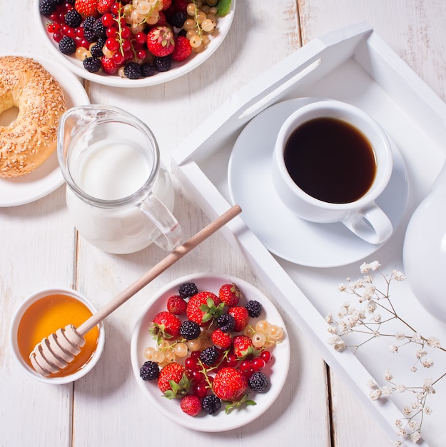 Bacche dolci fresche sul piatto bianco, bagel, tazza di caffè e miele per la prima colazione.