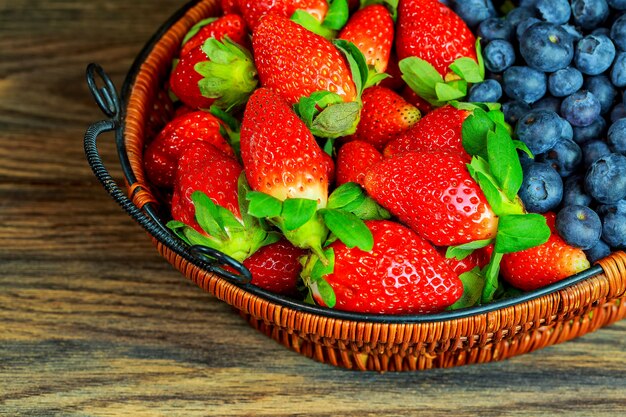 Bacche e fragole sane in un fondo di legno del canestro